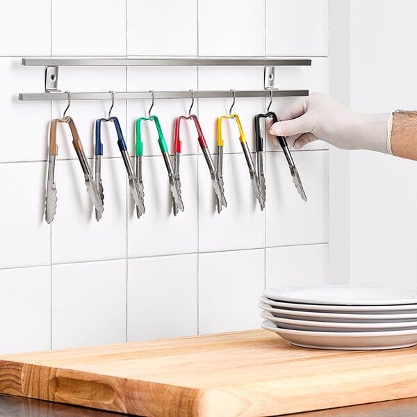 A person holding a pair of Vollrath Jacob's Pride tongs with multicolored handles.