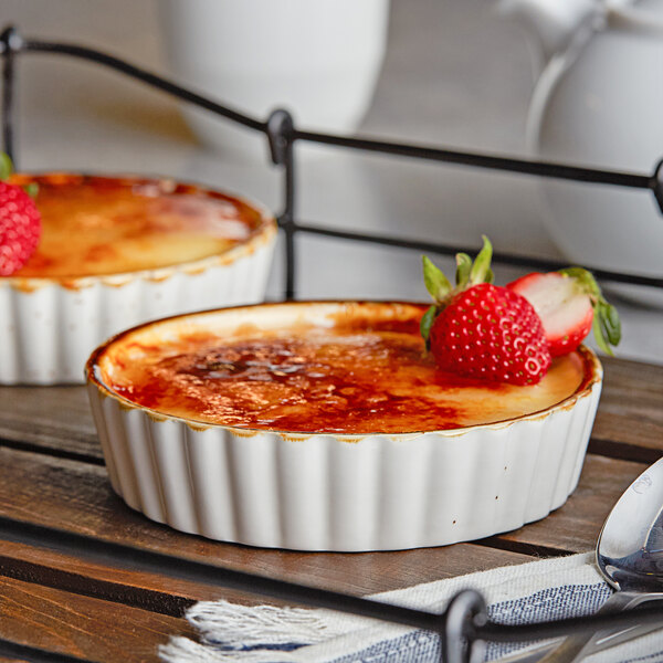 Two desserts in a white Acopa stoneware dish with a brown crust and strawberries on top.