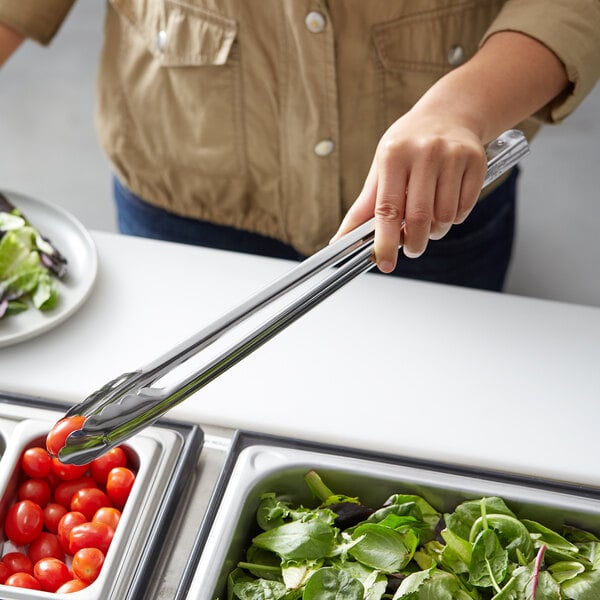 A person using Vollrath stainless steel tongs to serve cherry tomatoes at a salad bar.