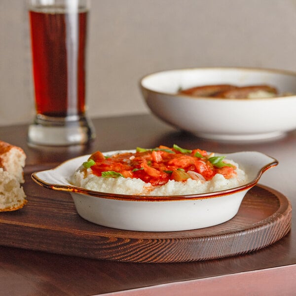 A bowl of mashed potatoes with tomato sauce in an Acopa Keystone stoneware dish on a wooden tray.