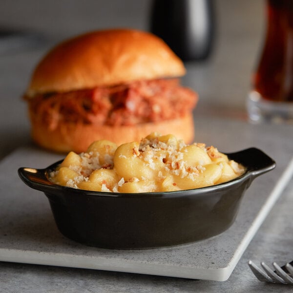 An Acopa Keystone stoneware rarebit dish filled with macaroni and cheese on a table next to a burger.