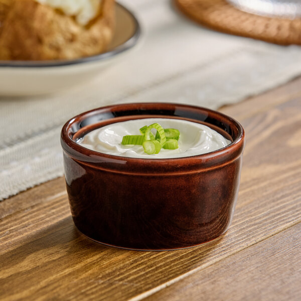 A brown stoneware ramekin filled with a creamy topping and garnished with chopped green onions.