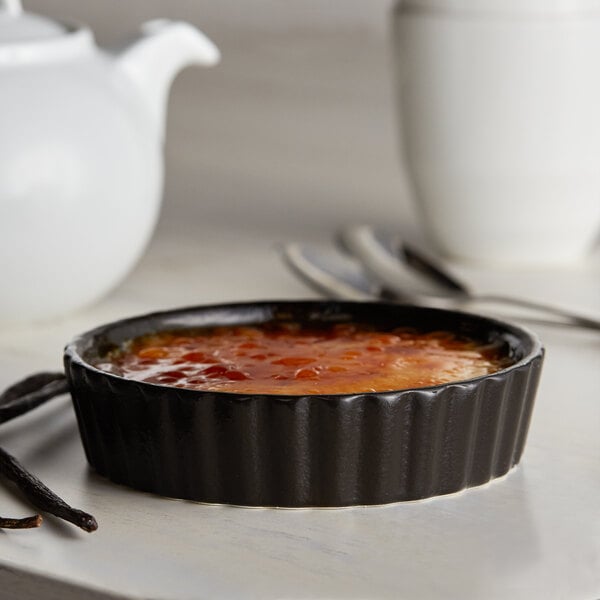 A small black Acopa stoneware dish with orange sauce and vanilla pods.