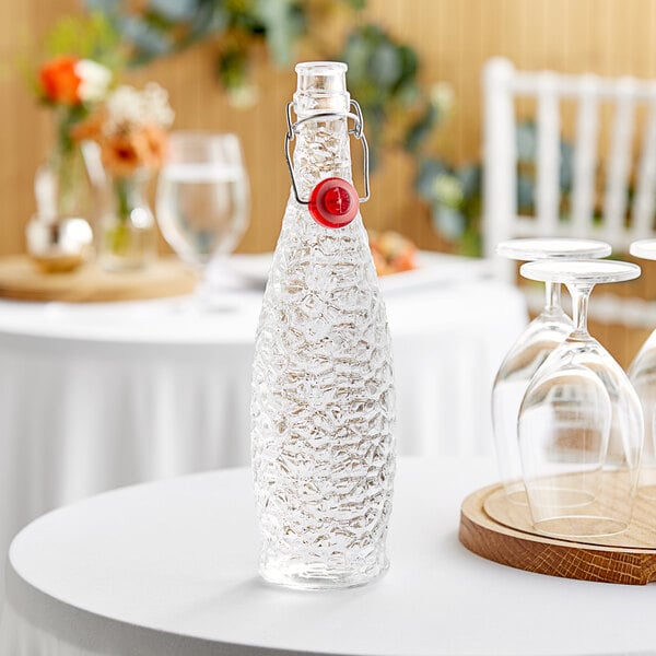 A Libbey glass water bottle with a red wire bail lid on a table.