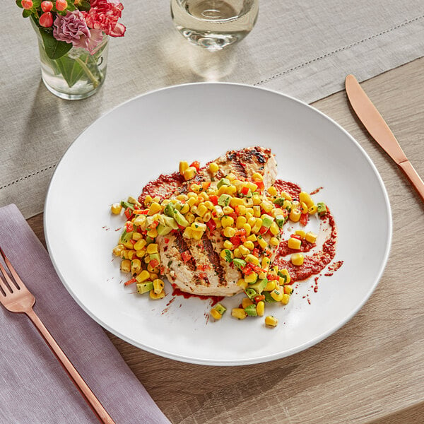 An Acopa Matte White Stoneware coupe plate with food, vegetables, and sauce on a table.