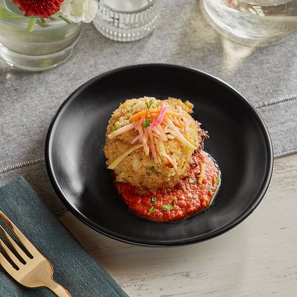 An Acopa matte black stoneware coupe plate with food and a fork on a table.