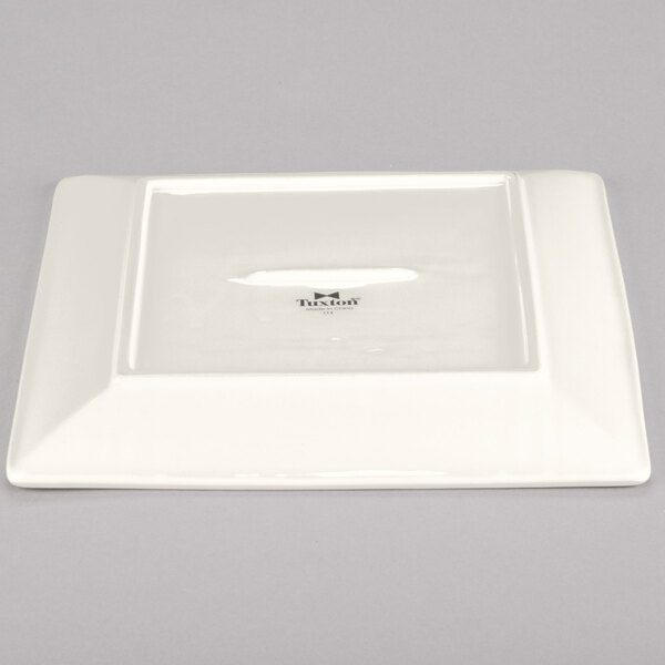 A white square plate with black text reading "Tuxton" on it.