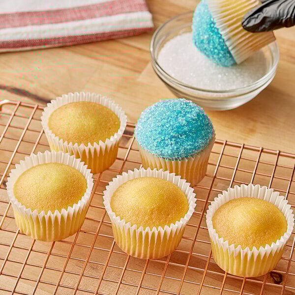 A hand putting yellow cupcakes with blue and white frosting in paper wrappers on a cooling rack.