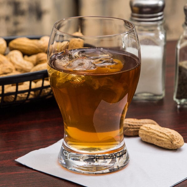 a glass of liquid with ice and a peanuts in the background