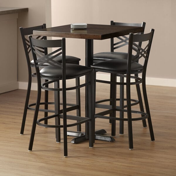 A Lancaster Table & Seating butcher block bar table with black chairs around it.