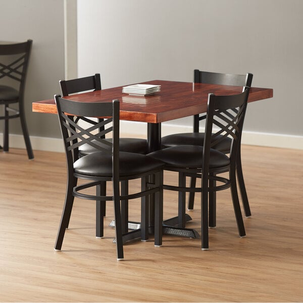 A mahogany Lancaster Table & Seating wood butcher block dining table with four black chairs around it.