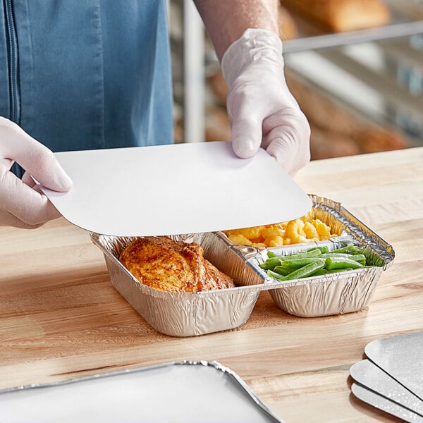 A person in gloves holding a Western Plastics 3-compartment foil tray filled with food.