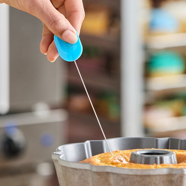 A cake tester with a blue handle being used to check the doneness of a cake in a bundt pan.