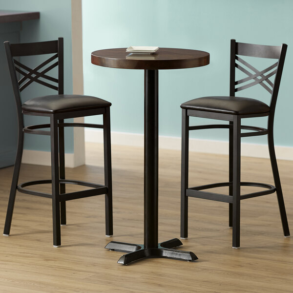 A Lancaster Table & Seating round wood table with two black chairs on a cast iron base.
