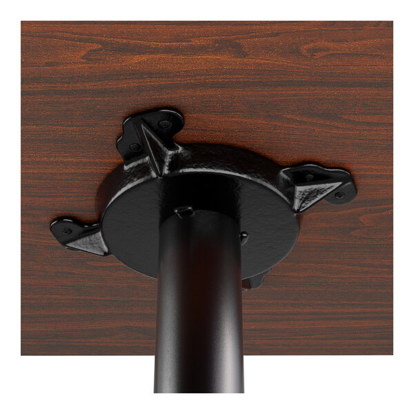 A close-up view of the underside of a wooden table top attached to a black metal pedestal base.