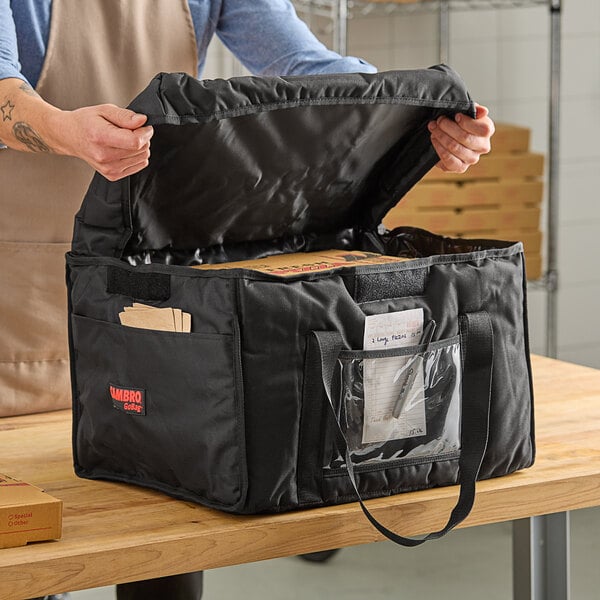 A person opening a black Cambro insulated delivery bag.