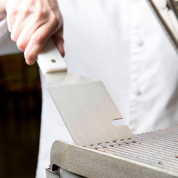 A hand holding a Star CG-S Panini Grill Spatula over a grill.