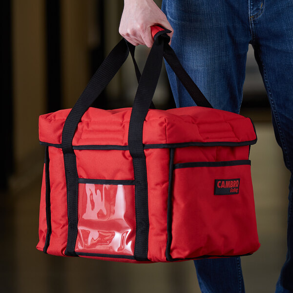 A man holding a red Cambro Sandwich GoBag with black straps.