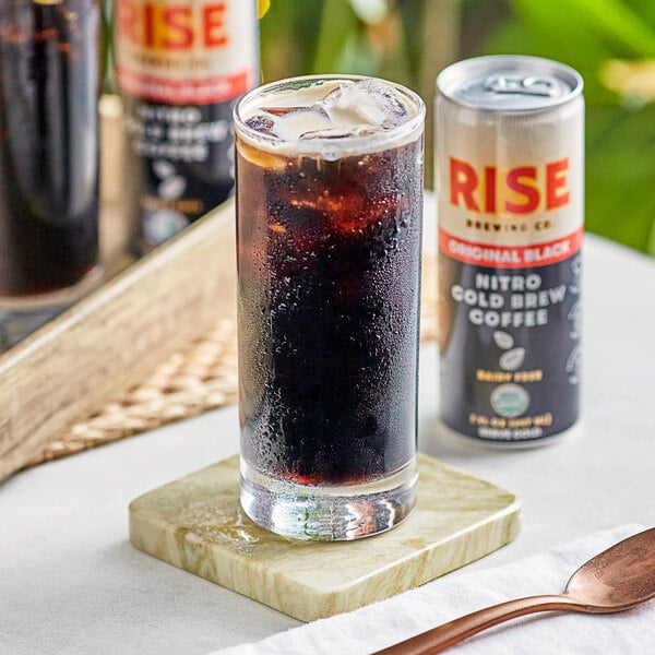 A glass of cold brew coffee with ice and a can of Rise Brewing Co. Organic Original Black Nitro Cold Brew Coffee on a table.