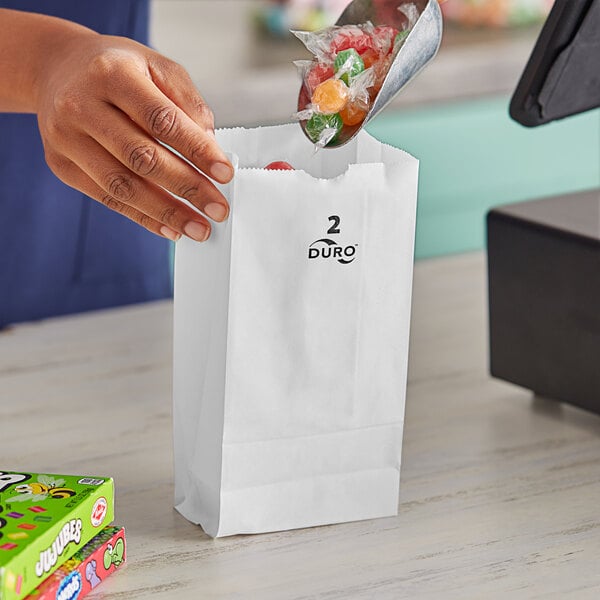 A hand putting candy in a white Duro paper bag.