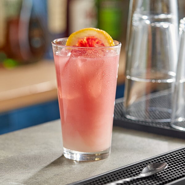 A glass of pink liquid with a slice of orange on top in a Anchor Hocking mixing glass.