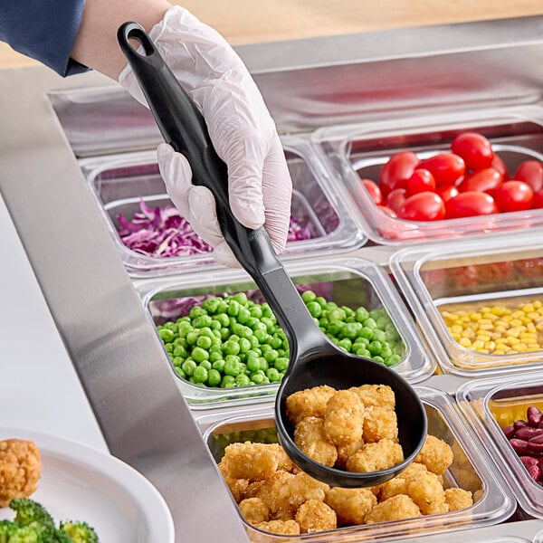 A person holding a black Vollrath Spoodle over food in a container.