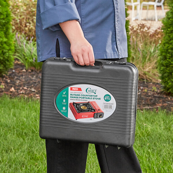 A person holding a black case with a red Choice portable stove inside.