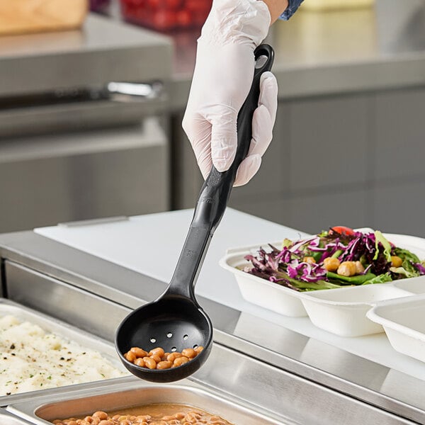 A person in gloves using a black Vollrath Spoodle to serve food from a white container.