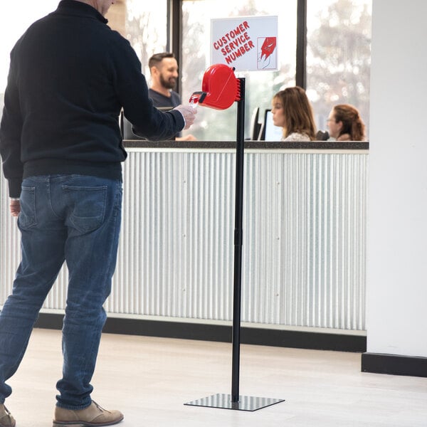 A man holding a red take-a-number dispenser with blue tickets.