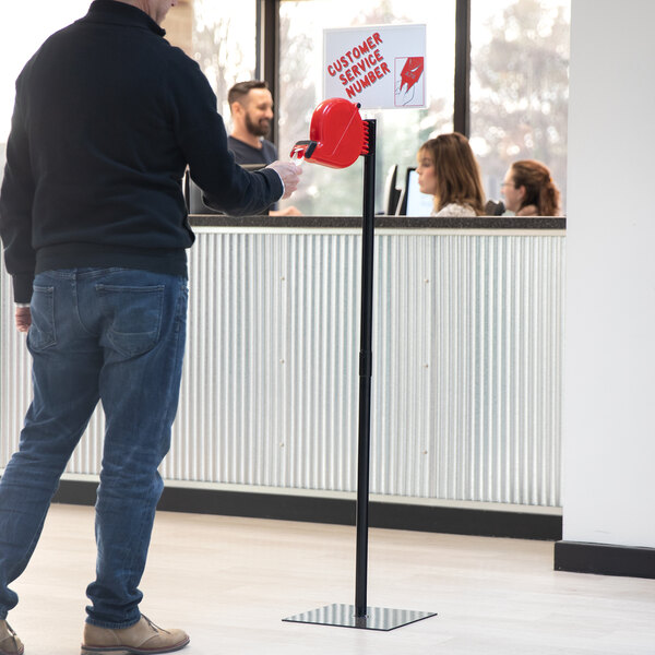 A man in a black sweater and jeans holding a red take-a-number ticket dispenser.