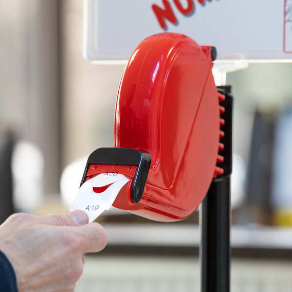 A person holding a red Garvey My Turn ticket dispenser with a white ticket in it.