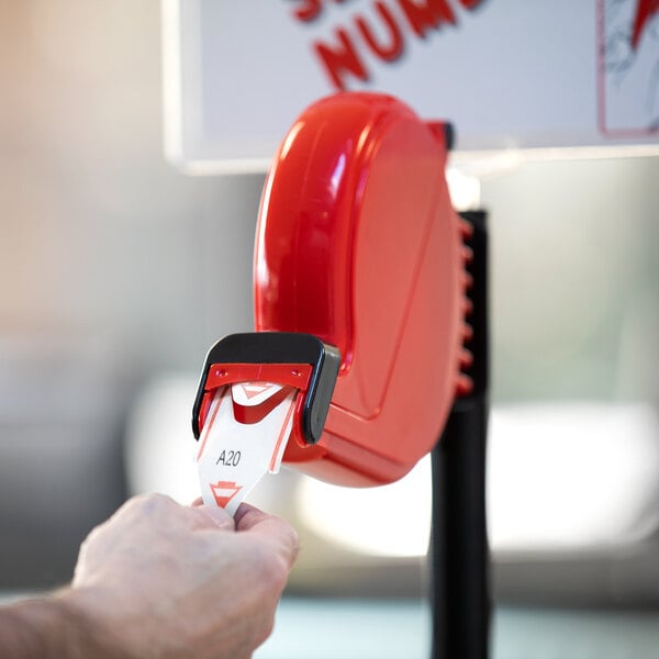 A hand holds a red Garvey My Turn ticket from a red ticket machine.