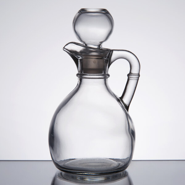 A clear glass cruet with a handle and a stopper.