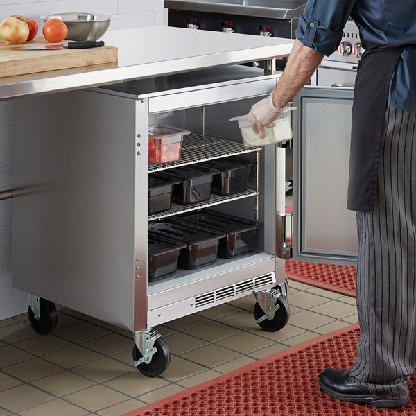 A person putting a container of flour into a Beverage-Air undercounter refrigerator.