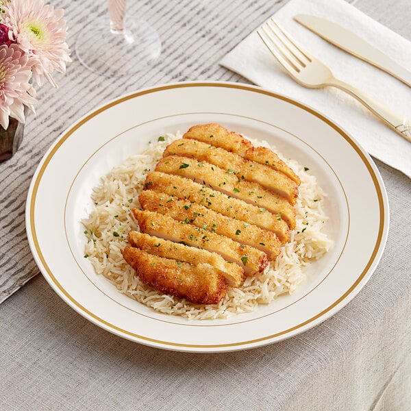 A WNA Comet ivory plastic plate with gold accent bands holding a meal of chicken and rice on a table with a drink and flowers.