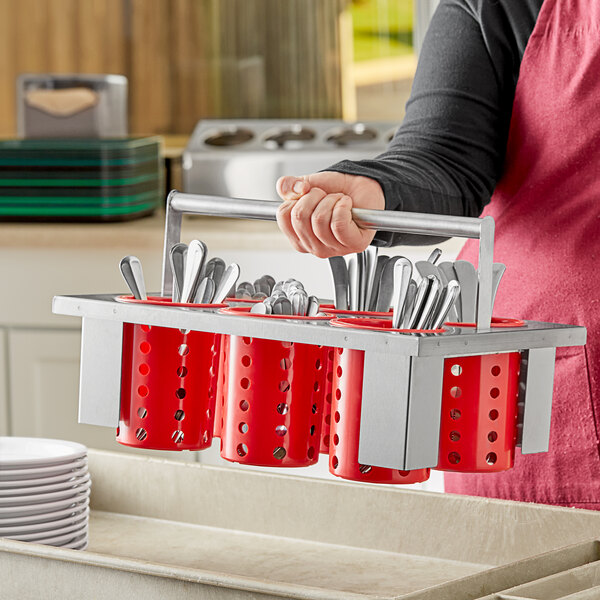 A woman holding a Steril-Sil stainless steel flatware basket with red plastic cylinders filled with utensils.