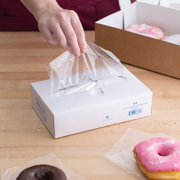 A hand using LK Packaging plastic deli wrap to put a donut into a box.