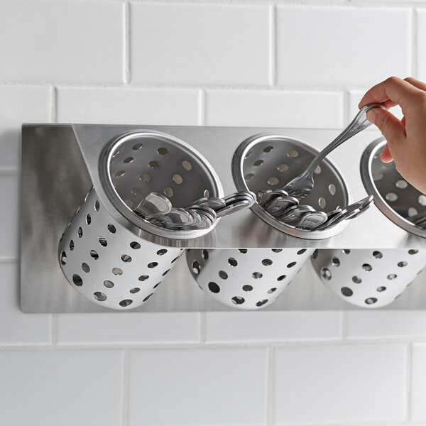 A hand holding a spoon in a Steril-Sil flatware container