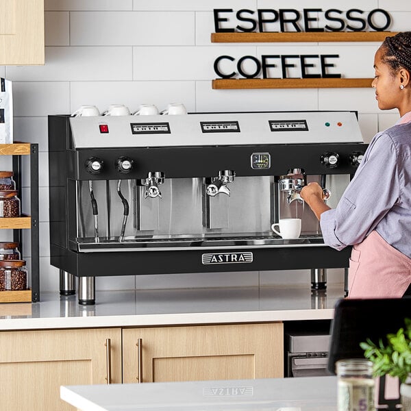 An Astra Mega III M3-013 automatic stainless steel espresso machine on a countertop in a coffee shop setting.