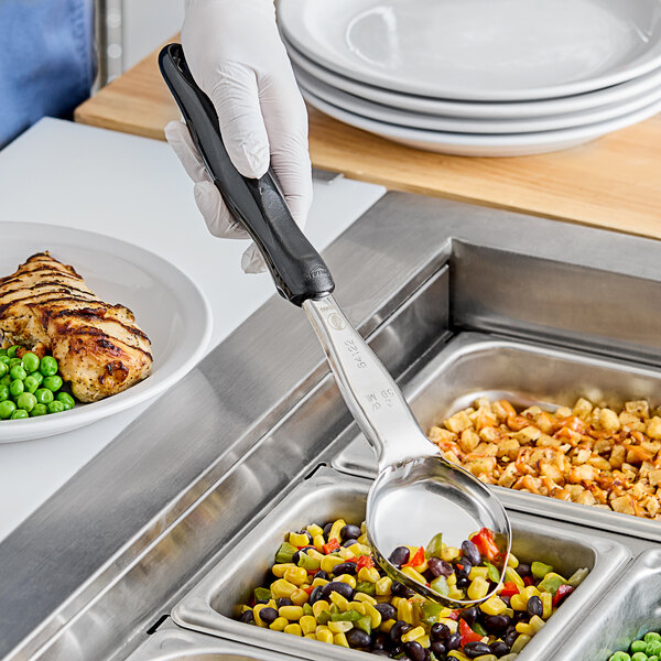 A hand in a glove holding a black Vollrath Spoodle over a bowl of food.