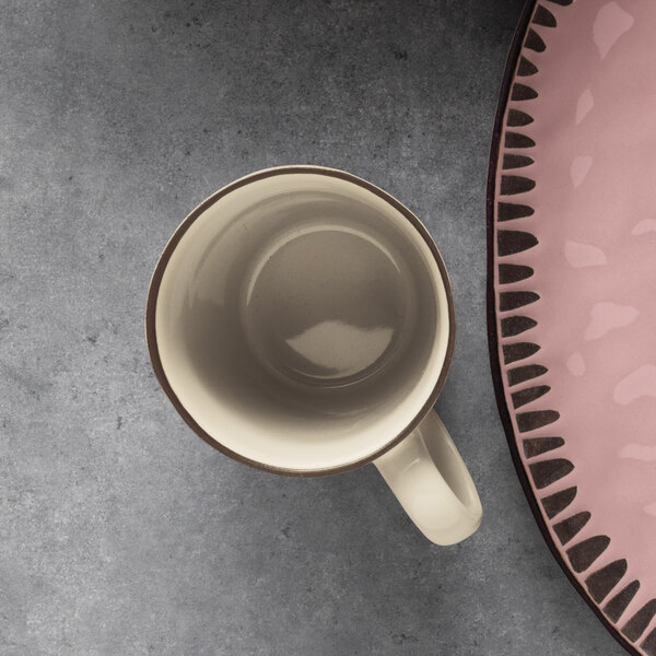 A Libbey cream stoneware mug next to a plate on a table.