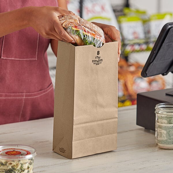 A woman holding a Duro Husky brown paper bag of food at a register.