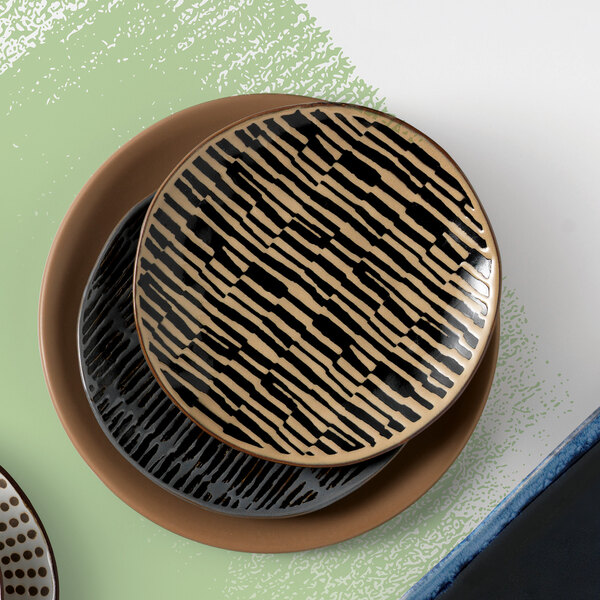 A stack of World Tableware Afar stoneware salad plates with a brown and black pattern on a table.