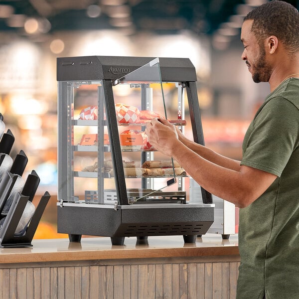 A man opening a countertop heated display case with food inside.