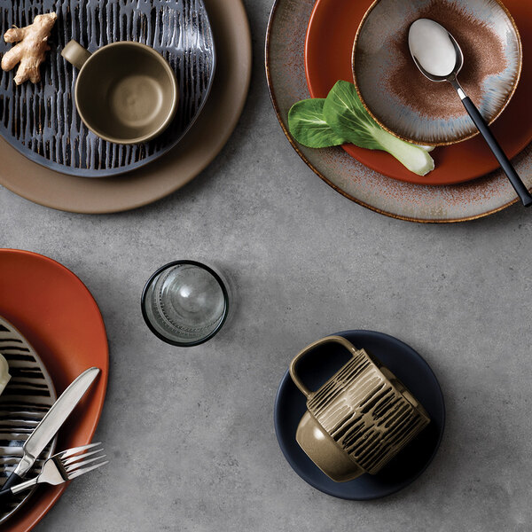 A brown World Tableware Afar stoneware mug on a table with plates and utensils.