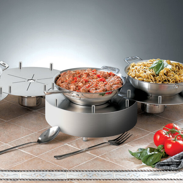 Stainless steel trays of food on a table in an outdoor catering setup.