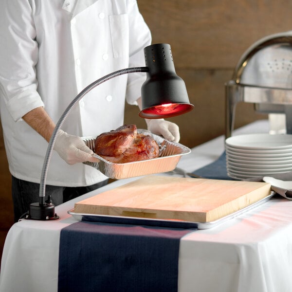 A chef using an Avantco carving station heat lamp to serve a turkey on a table.