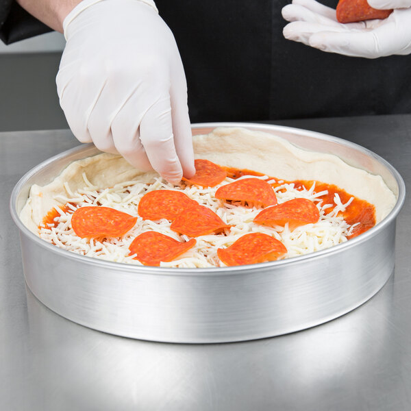 A person wearing gloves preparing a pizza in an American Metalcraft aluminum cake pan.