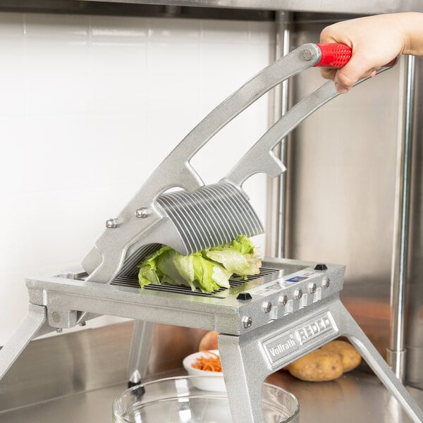 A person using a Vollrath Redco vegetable cutter to slice lettuce.