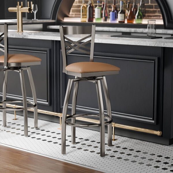 A metal bar stool with a cross back design and a light brown vinyl padded seat, featuring a swivel function.